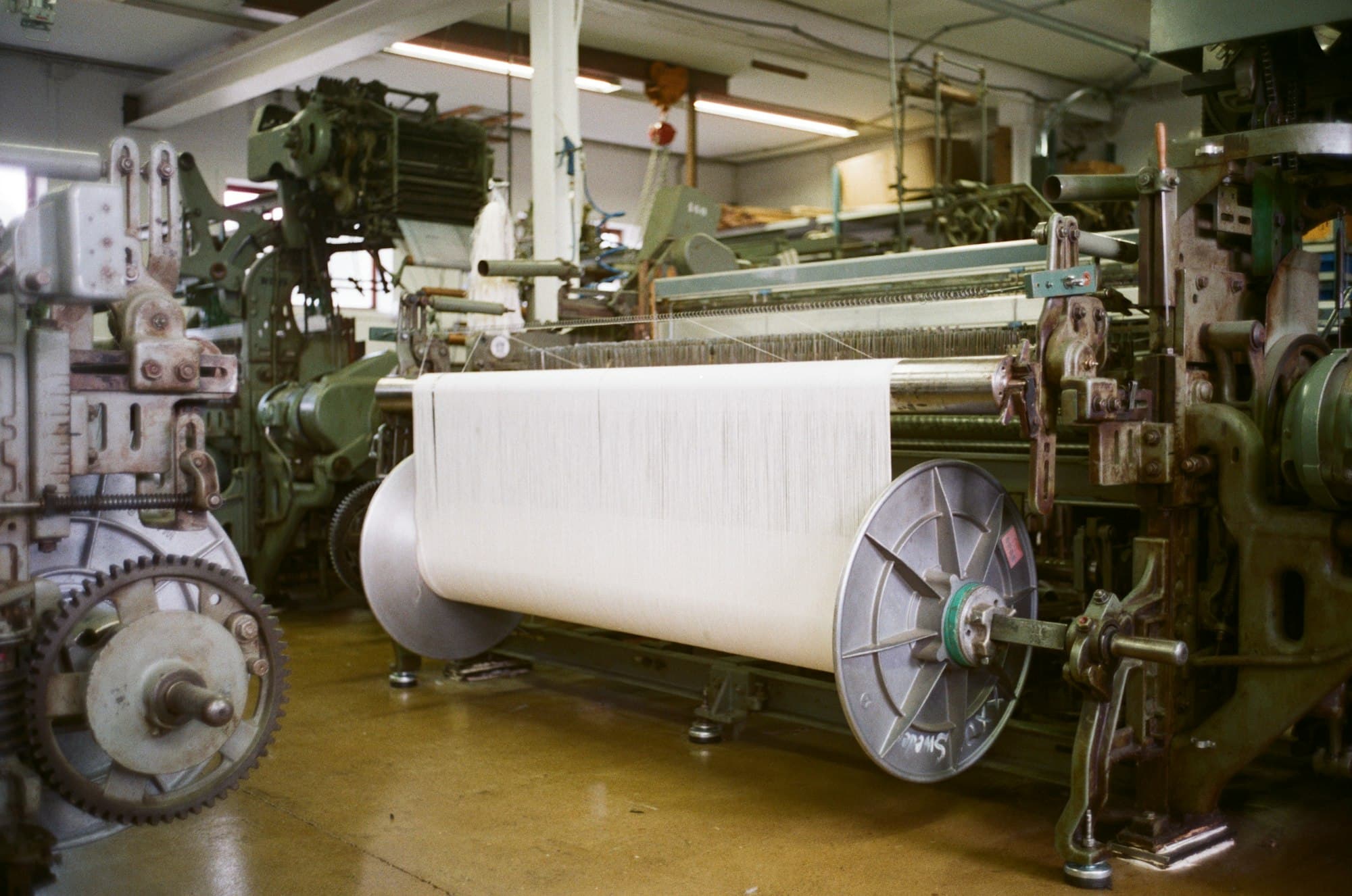 An industrial loom weaving natural fibre cloth on a factory floor